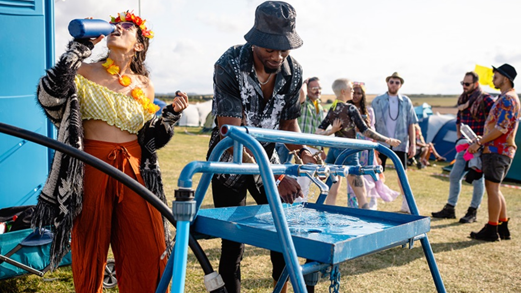 A man and a woman at a mobile water dispenser at a festival.