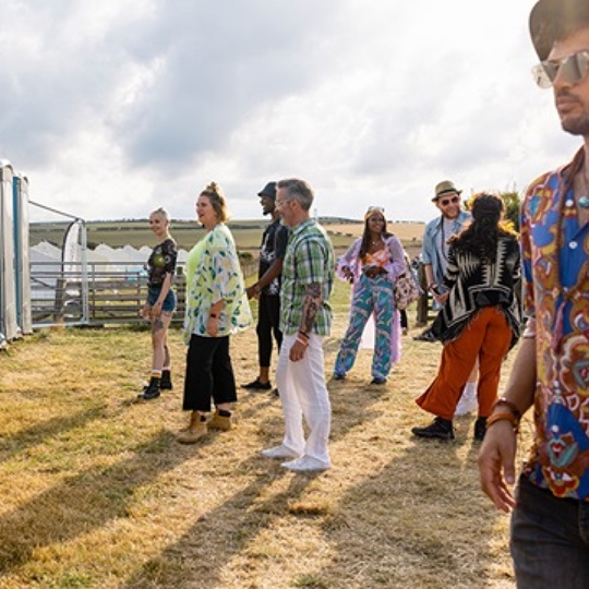 Several people queue up in front of porta-potties at a festival.