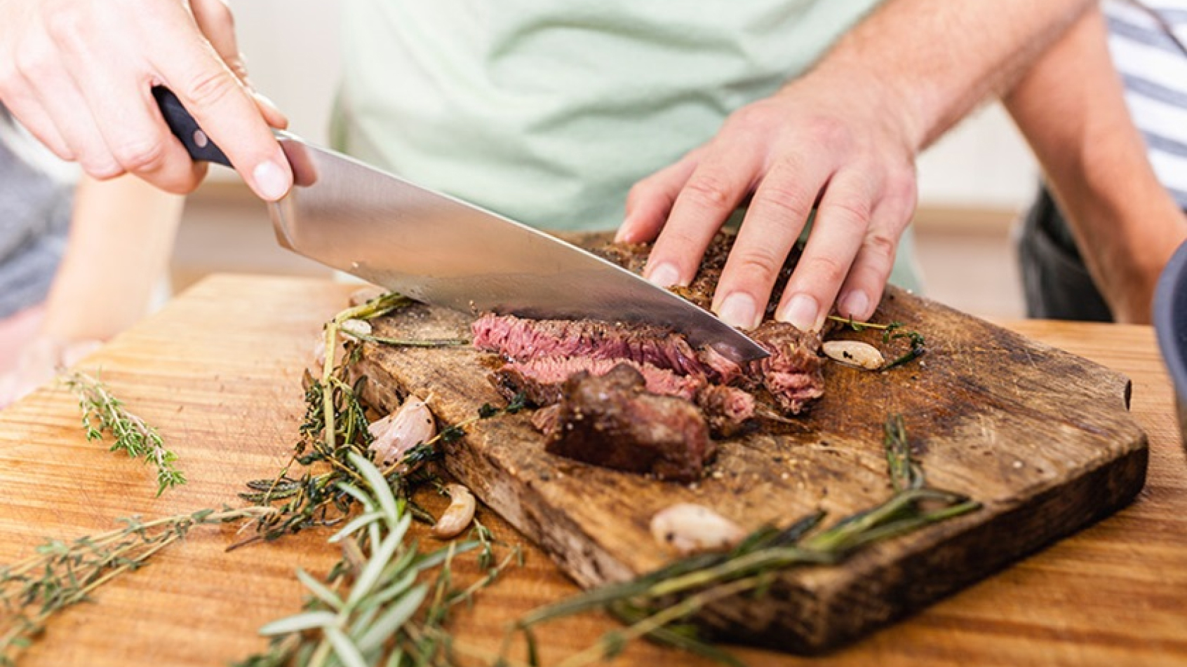 Photo of a wooden board and someone cutting meat. 