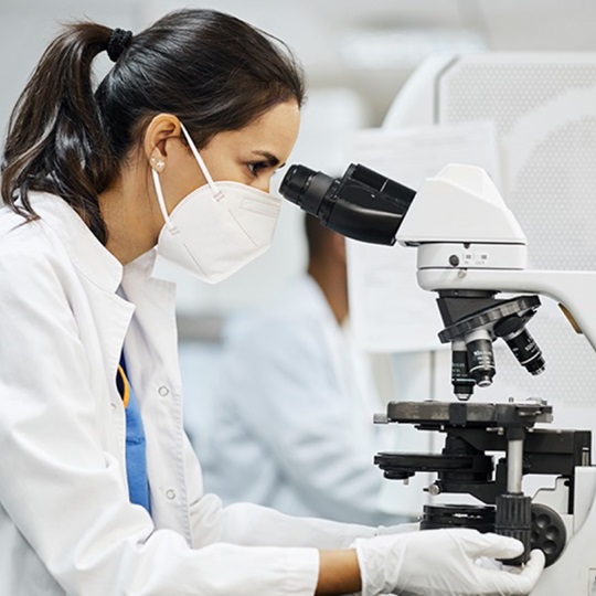 A researcher in a white coat looks into a microscope.