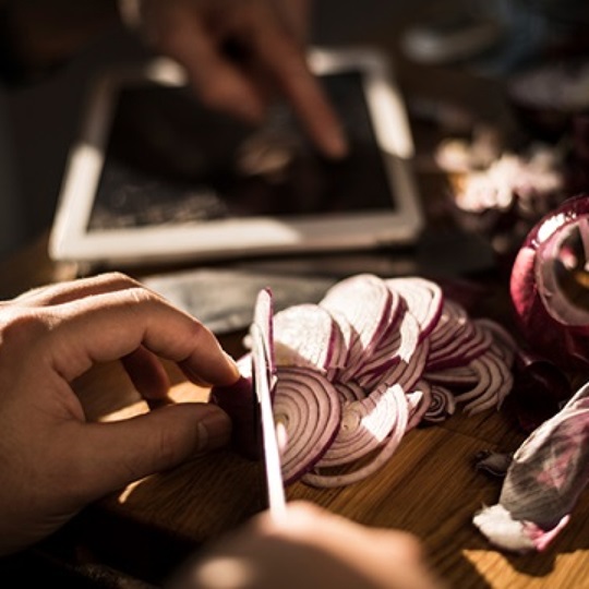 Close up of onions being cut on wooden board in kitchen.