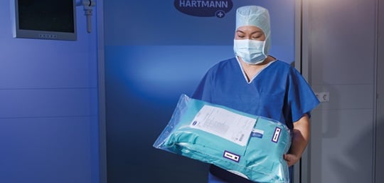 Pflegekraft trägt in Folie verpacktes OP-Set in den OP
