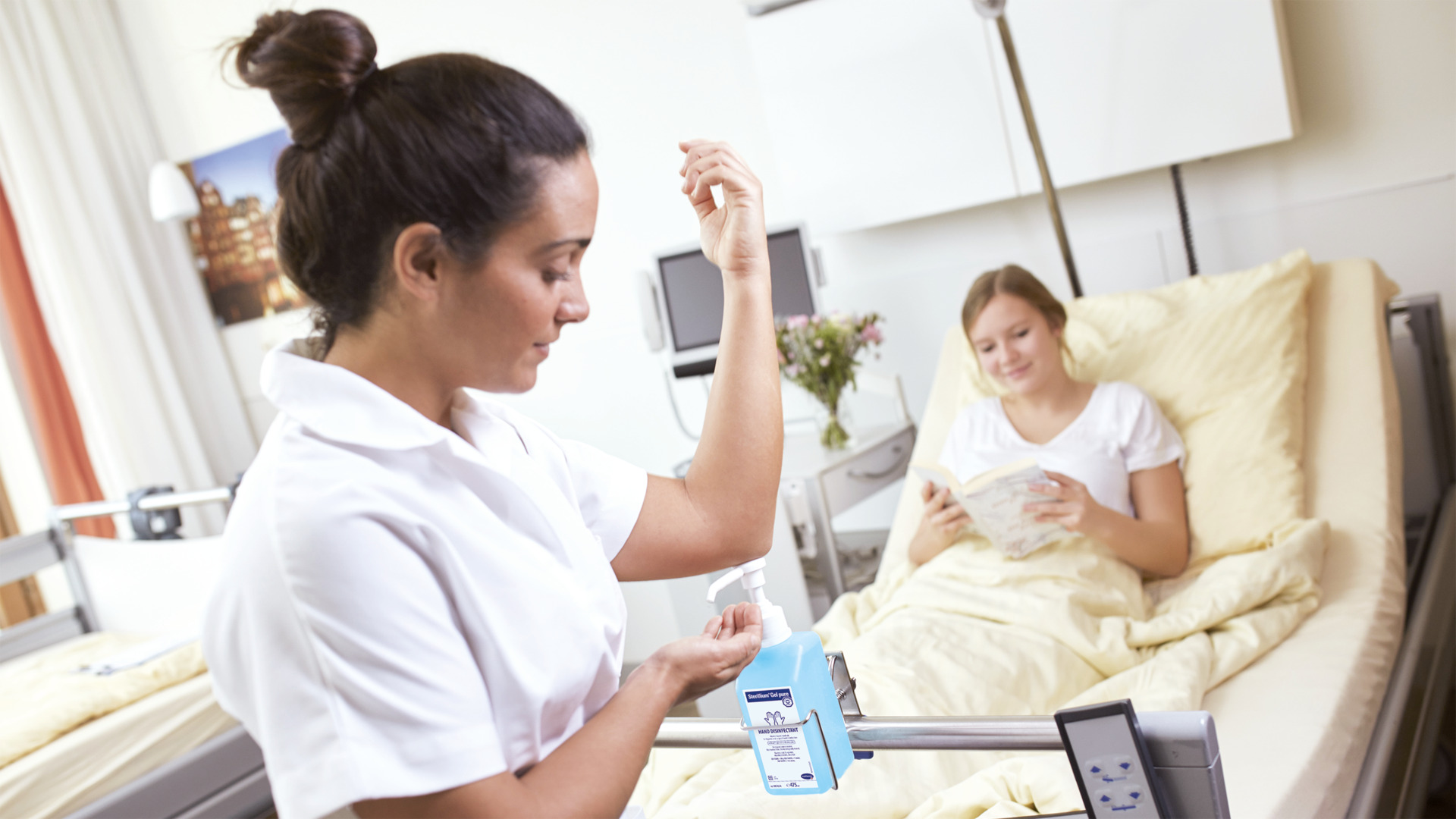  Nurse uses hand sanitizer in a hospital room while a patient relaxes in bed, highlighting hygiene in patient care settings.