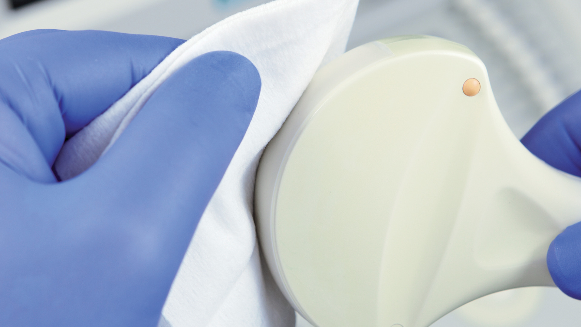  Gloved hands carefully cleaning an ultrasound probe with a soft white cloth, emphasizing precision and hygiene in medical equipment care.