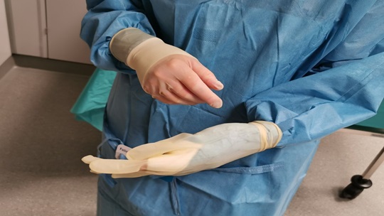 Die Abbildung zeigt, wie die Stulpe hochgezogen und die Finger in den Handschuh eingeführt werden.
