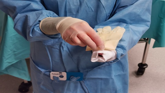 Die Abbildung zeigt, wie die Finger in die Öffnung des Handschuhs eingeführt werden.
