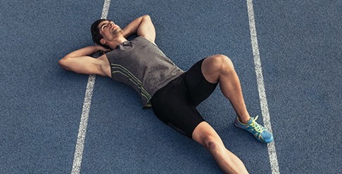 Mladý muž v športovom ležiaci na bežeckej dráhe.