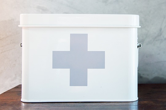 White first aid box with grey cross on wooden cupboard in front of whit marble wall.