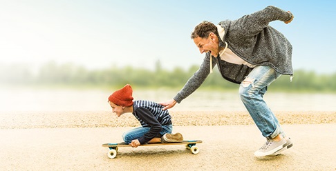 Father running and speeding son kneeling on skateboard.