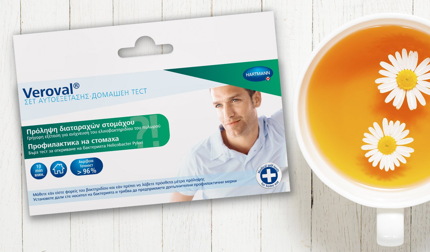 Eine Packung des Veroval® Selbst-Tests zur Magenvorsorge liegt auf einer weißer Holzoberfläche neben einer Tasse Tee.