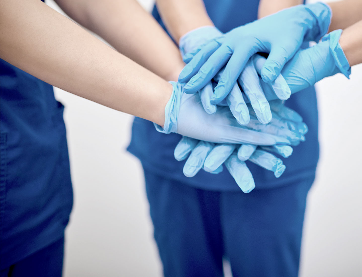Personál nemocnice so zdravotníckymi rukavicami na rukách stojí v polkruhu a majú položené ruky na sebe 