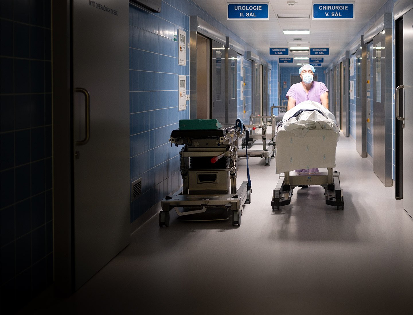 Nurse in full protective clothing pushing patient’s bed through hospital corridor