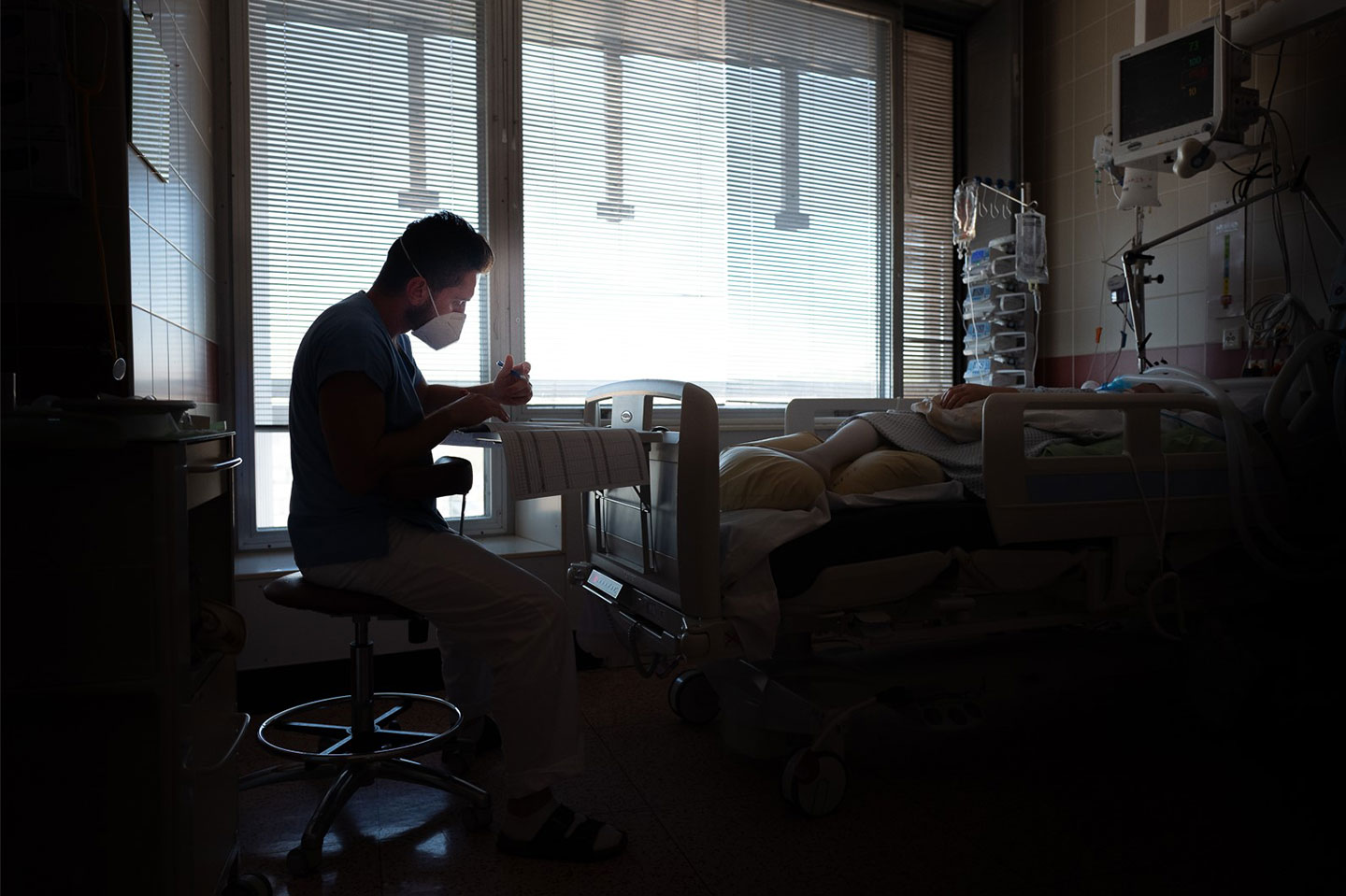 Nurse in dark hospital room filling out files next to patient’s bed