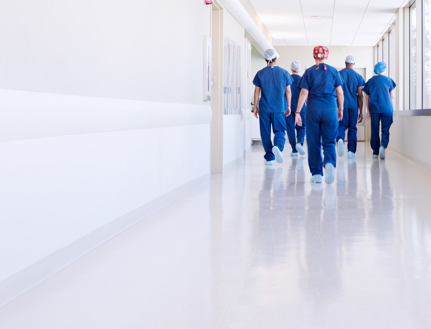 Image of nurses dressed in blue protective clothing walking down a hospital corridor