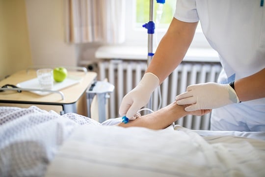 Nurse performing peripheral venous catheterization on patient in hospital bed