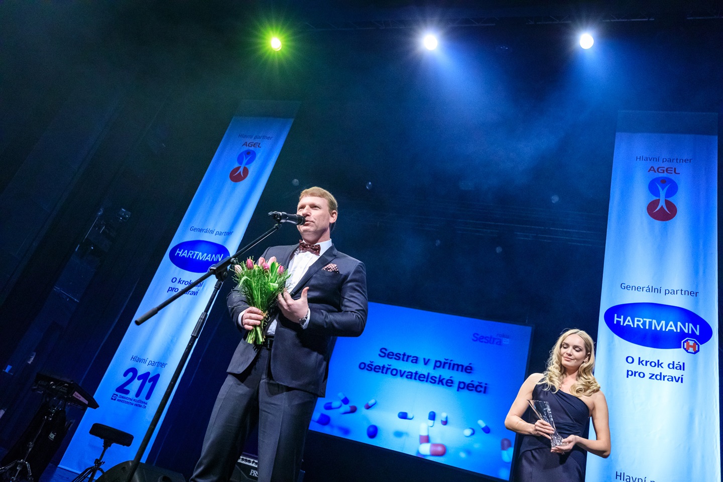 U mikrofonu Tomáš Groh, Managing Director HARTMANN-RICO a Taťána Gregor Brzobohatá vyhlašují na pódiu divadla Hybernia vítězku kategorie Sestra v přímé ošetřovatelské péči