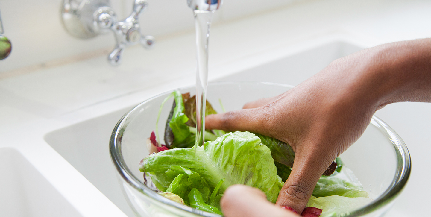 Ausschnitt einer Küchenspüle, in der Hände Salatblätter reinigen