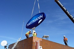 Instalace velkého loga HARTMANN v modrém oválu na střechu budovy s pomocí jeřábu je důkazem, že akvizice společnosti Lindor ve Španělsku dopadla dobře.