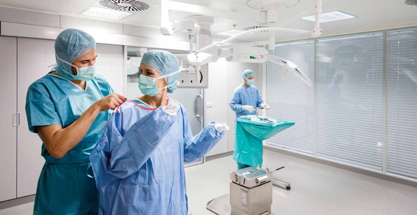 Momentka z přípravy na operaci. Lékař pomáhá kolegyni do chirurgického pláště.