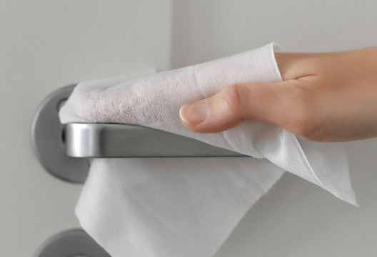 Eine Hand desinfiziert mit einem Desinfektionstuch eine Türklinke.