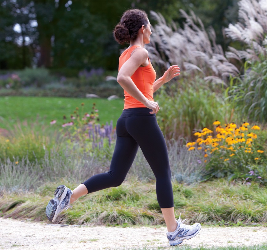 A woman, dressed in sport clothes, is jogging in a flourish park.