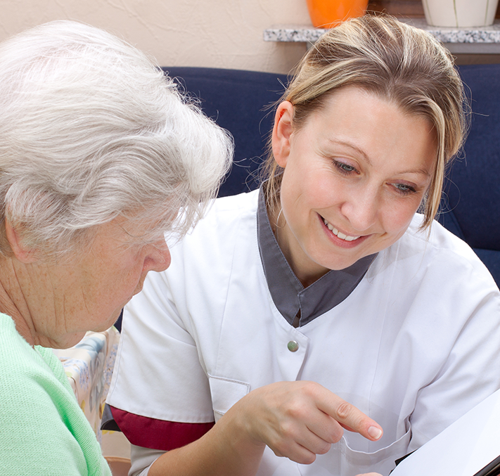 Pflegerin zeigt Seniorin Informationen auf Klemmbrett 
