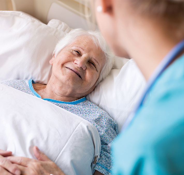Pflegerin am Bett einer lächelnden Seniorin