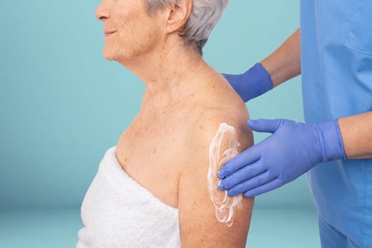Pflegerin cremt Arm einer Seniorin ein