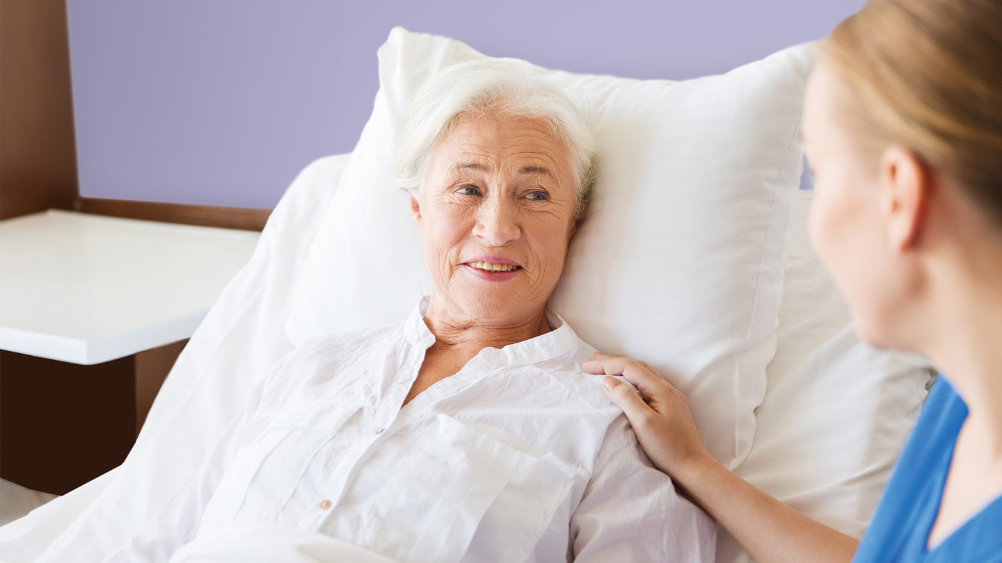 Pflegerin sitzt neben Seniorin im Bett