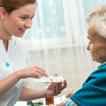 Pflegerin zeigt Seniorin Medikamente in der Medikamentenbox