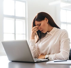 gestresste Frau am Arbeitsplatz vor Laptop