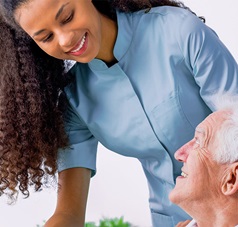 Pflegerin beugt sich über lächelnden Senior der am Tisch sitzt
