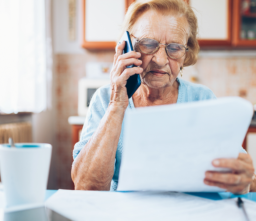Seniorin am Telefon mit Unterlagen vor sich