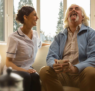 Krankenschwester lacht mit Patientem auf dem Sofa