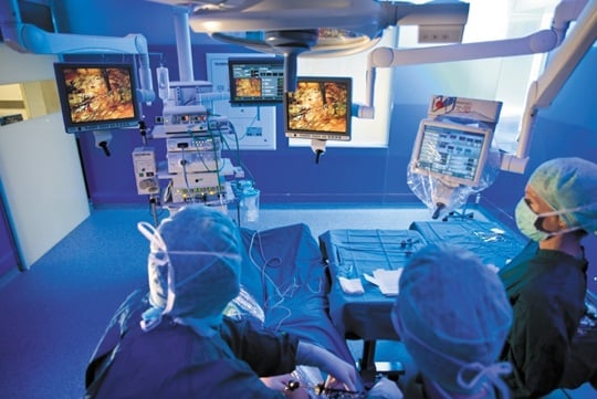 Drie artsen zijn in een operatiezaal aan het opereren en kijken naar hun monitors.