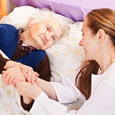 Frau am Bett die Hand einer Seniorin