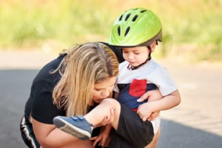 Maminka fouká dítěti koleno po pádu z kola