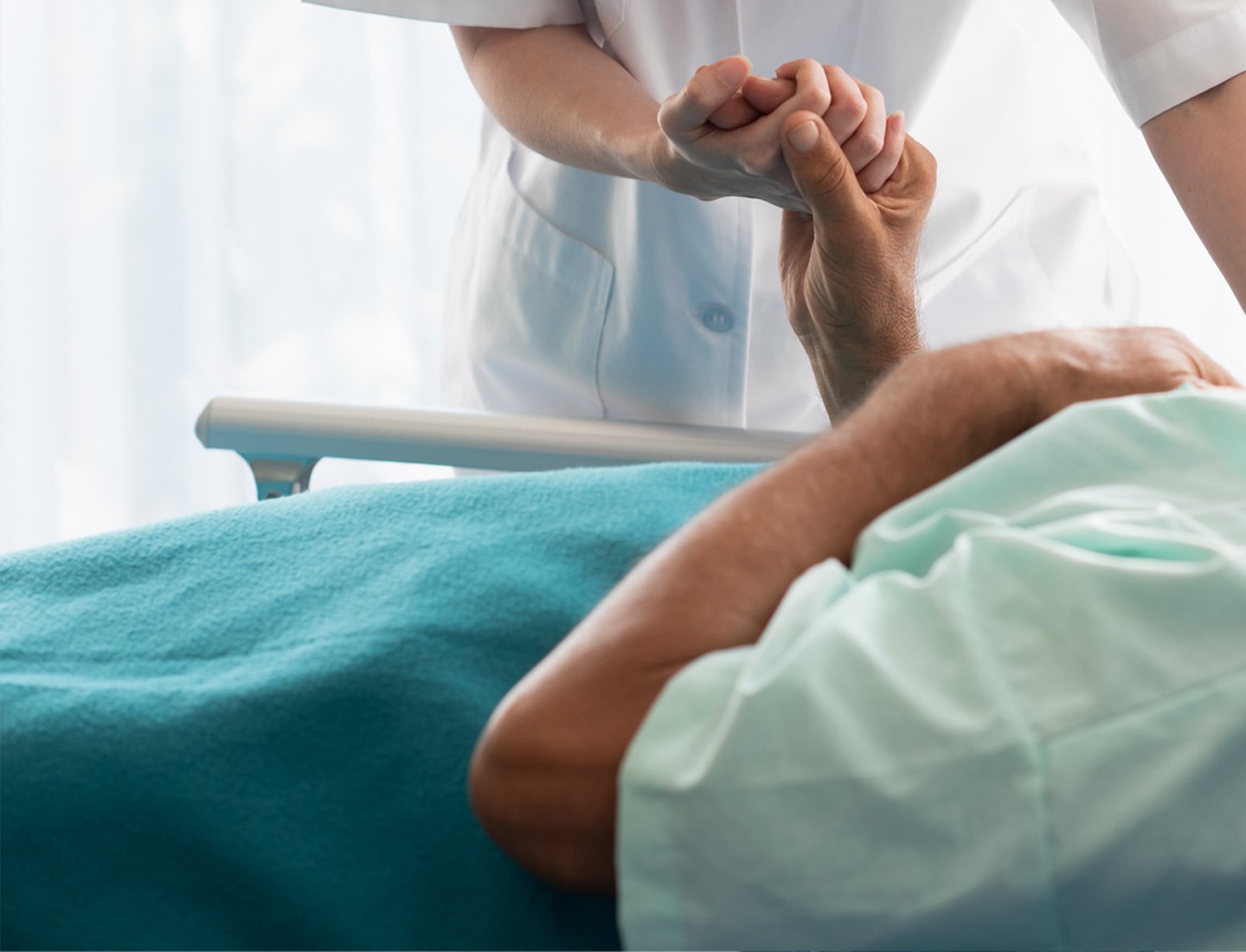 Pflegerin hält Hand einer im Bett liegenden Seniorin
