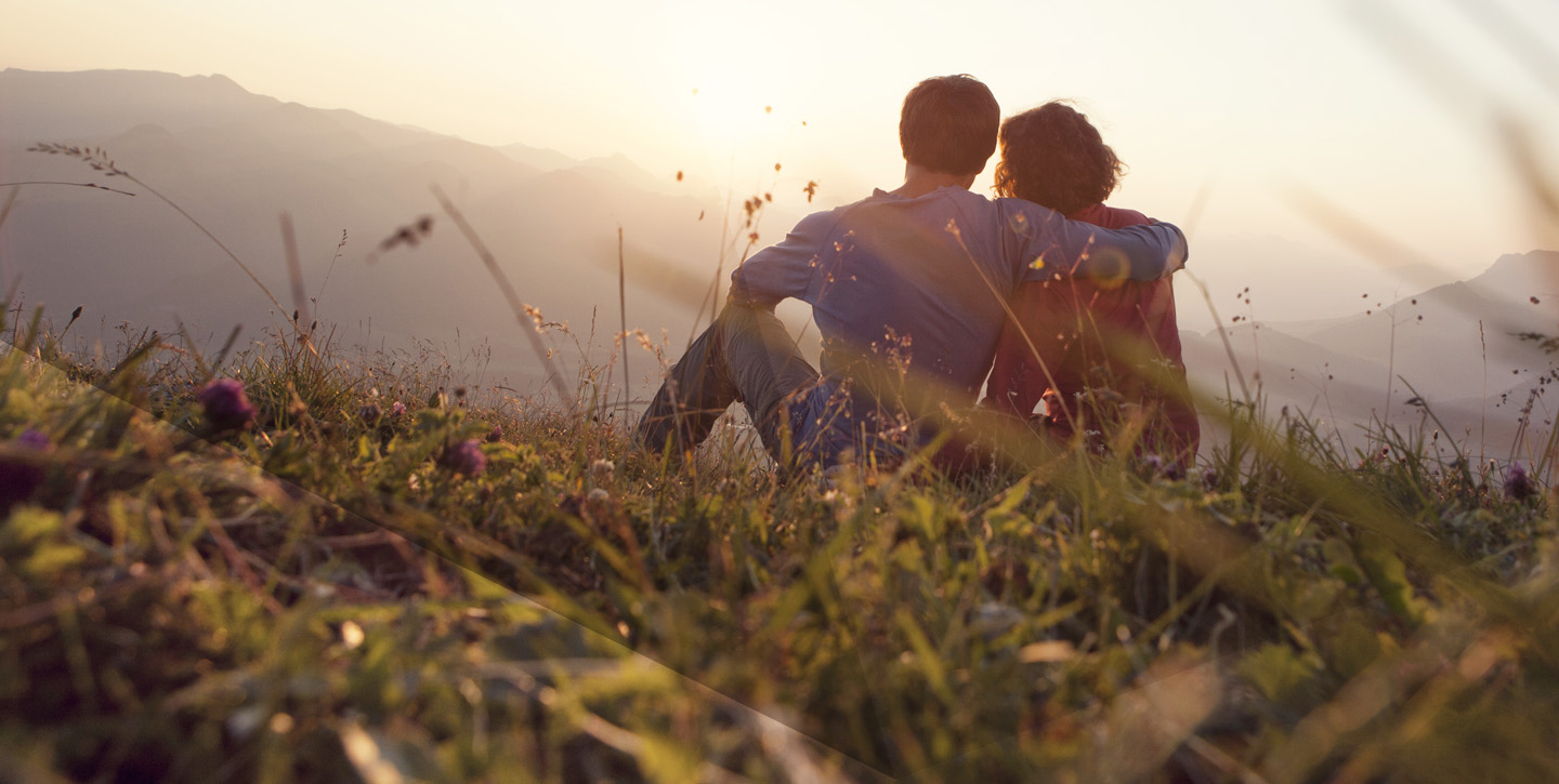 Couple sat on top of a mountain field full of long grass