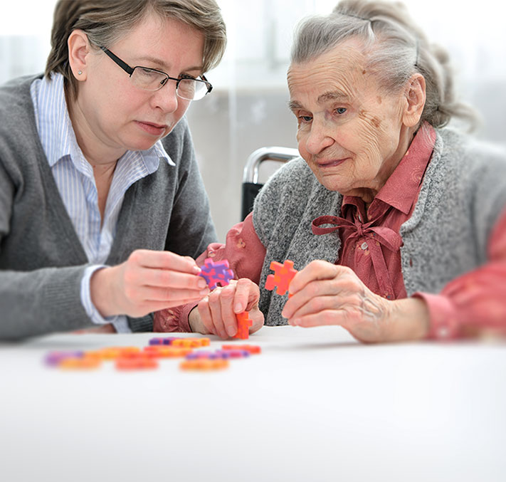 Pflegende Angehörige mit Seniorin bei einem Spiel