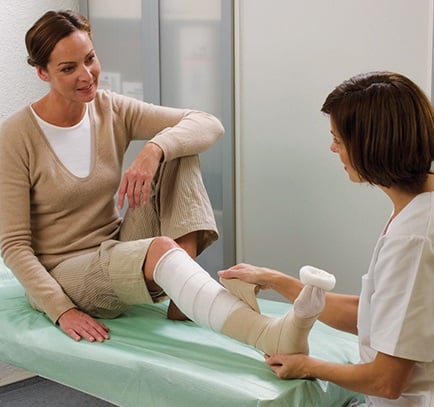 A nurse is treating the wound on a woman’s foot