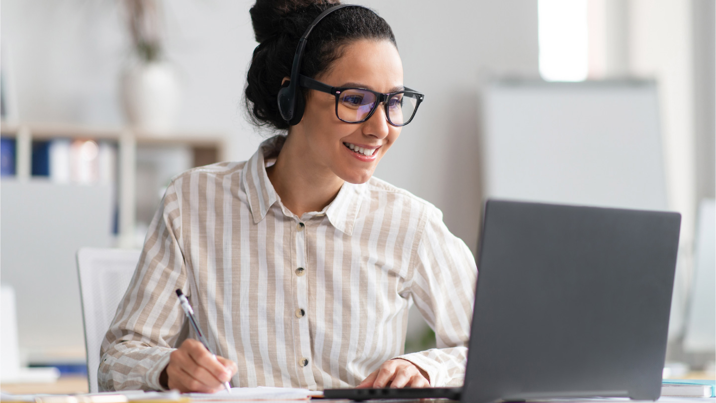Portrait of happy young woman wearing wireless headphones watching online course, sitting at table
