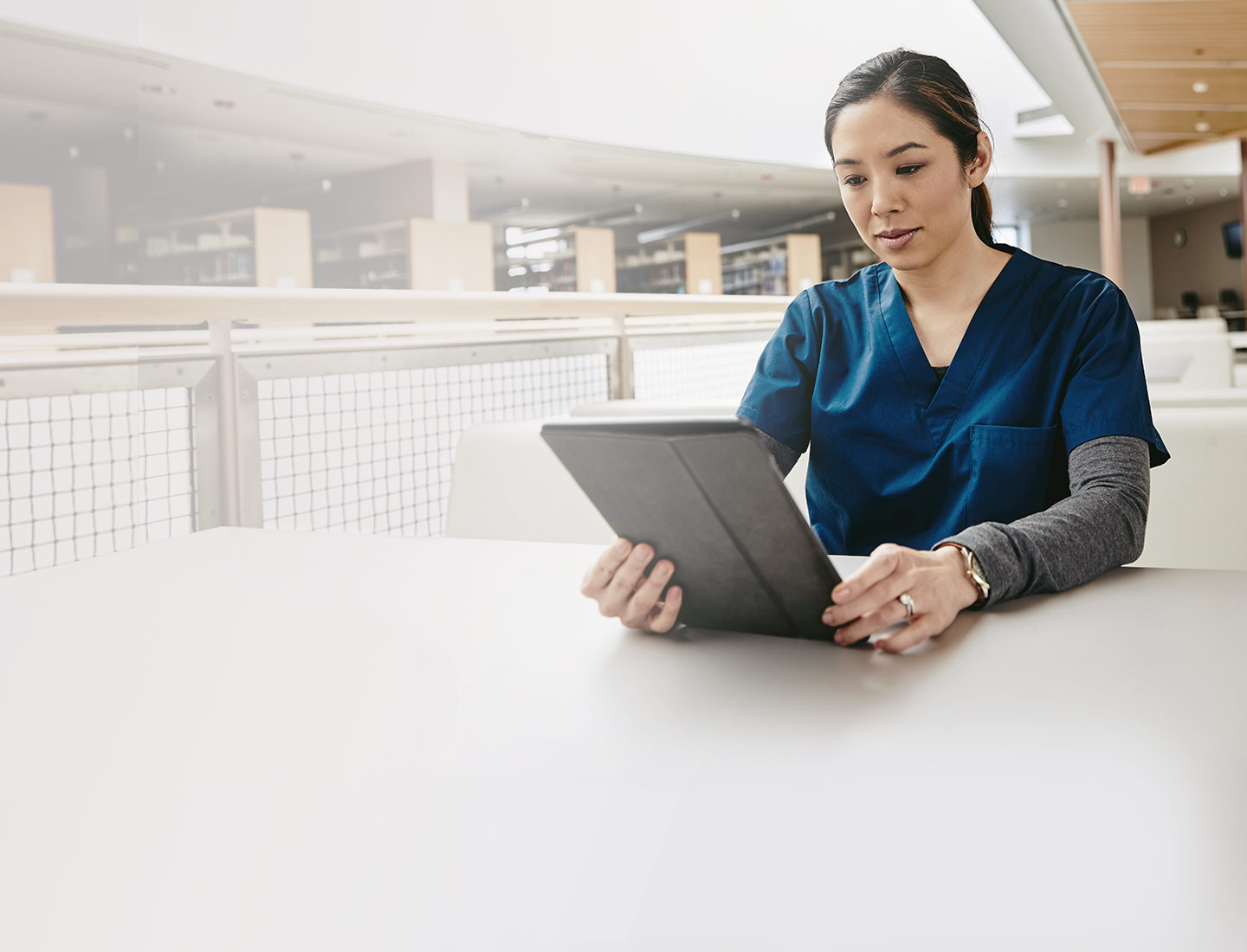 Woman in a tunic sits at the table and looks into a tablet