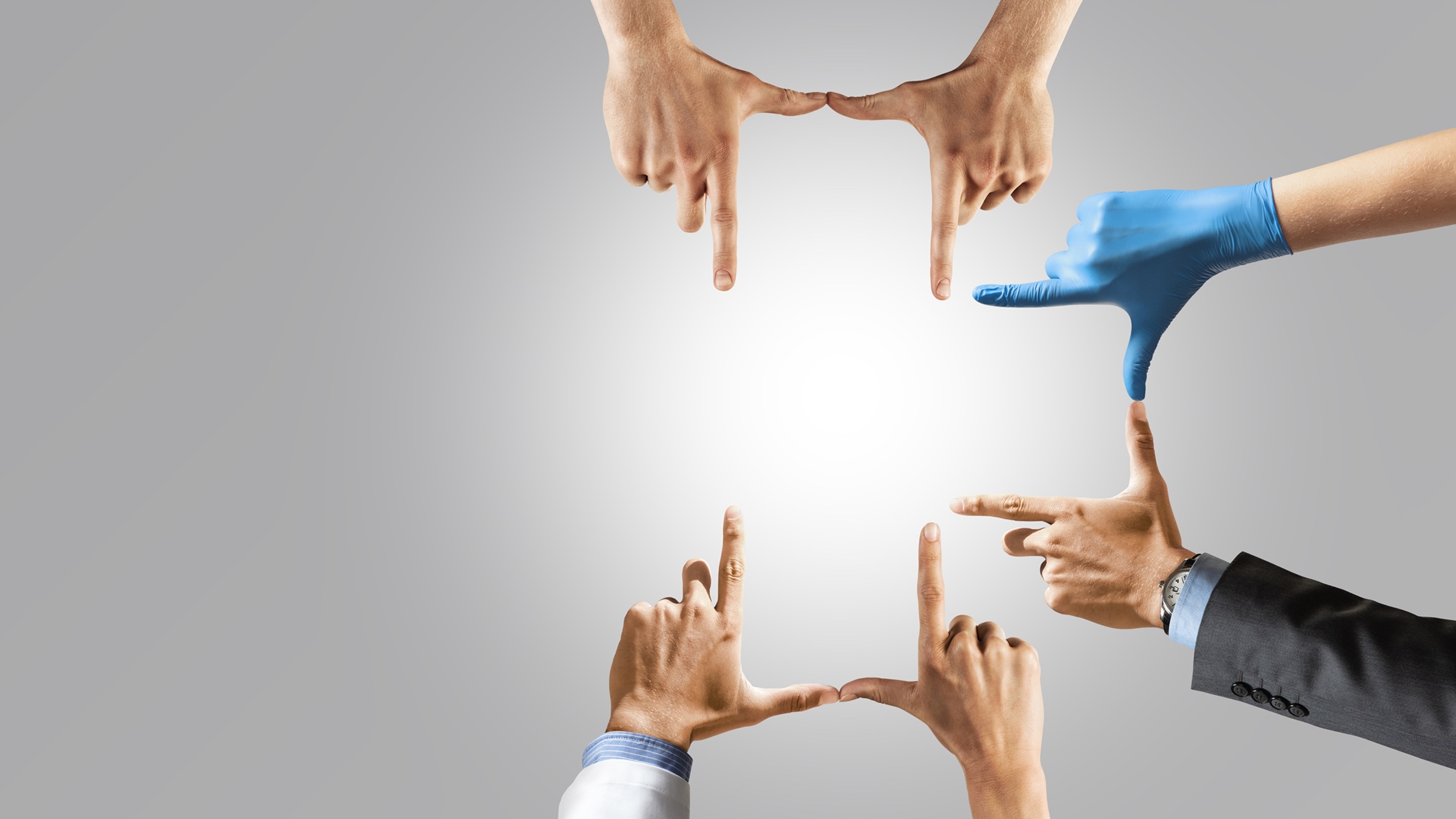 Six hands from different people and dressed in different attire. are positioned to form a frame around a blank space.
