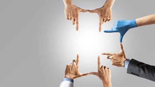 Six hands from different people and dressed in different attire. are positioned to form a frame around a blank space.