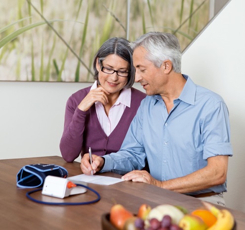 elderly couple sitting on a table with a blood pressure monitor writing something down